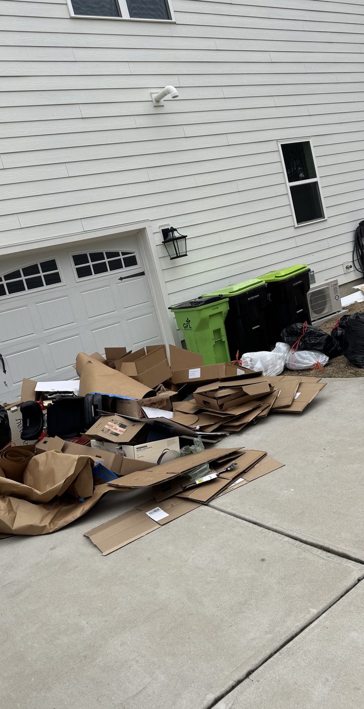 Driveway piled with cardboard boxes, bags, and household junk — before Junk Doctors